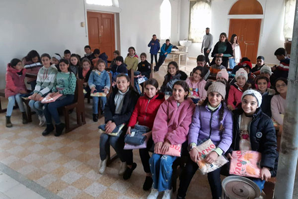 Schulkinder sitzen in einem Raum, sie haben alle einen noch eingepackten Pulli auf dem Schoß