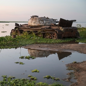 Ein verrosteter Panzer steht an einem Flussufer.